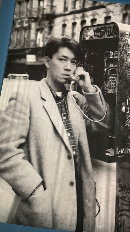 外国で公衆電話の受話器をとる若かりし頃の坂本龍一のモノクロ写真